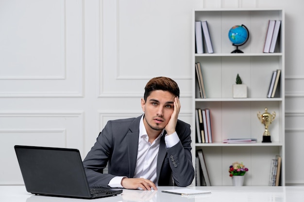 Customer service cute handsome guy in office suit with computer tired with the hand on temples