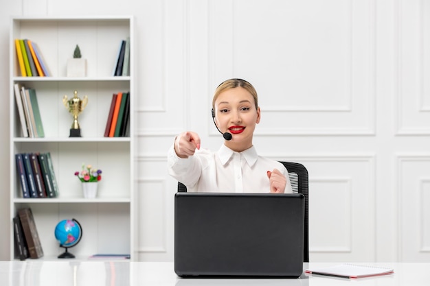 Customer service cute woman in white shirt with headset and computer pointing front and smiling