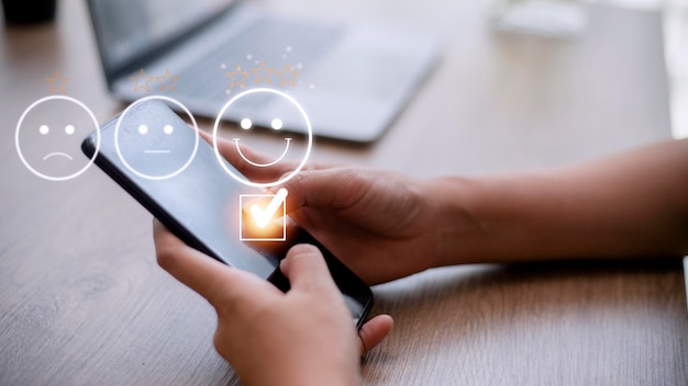 customer service evaluation concept using a smartphone is pressing face emoticon smiling in satisfaction on virtual touch screen