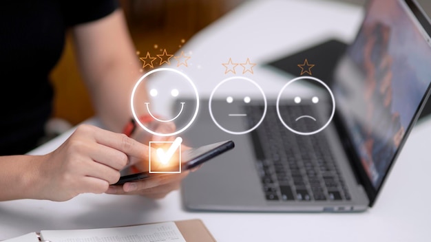 customer service evaluation concept using a smartphone is pressing face emoticon smiling in satisfaction on virtual touch screen