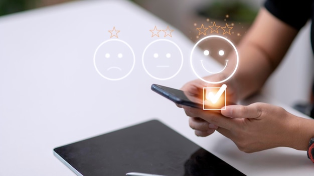 Customer service evaluation concept using a smartphone is\
pressing face emoticon smiling in satisfaction on virtual touch\
screen