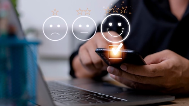 Customer service evaluation concept using a smartphone is pressing face emoticon smiling in satisfaction on virtual touch screen