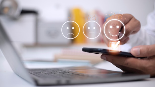 Photo customer service evaluation concept using a smartphone is pressing face emoticon smiling in satisfaction on virtual touch screen