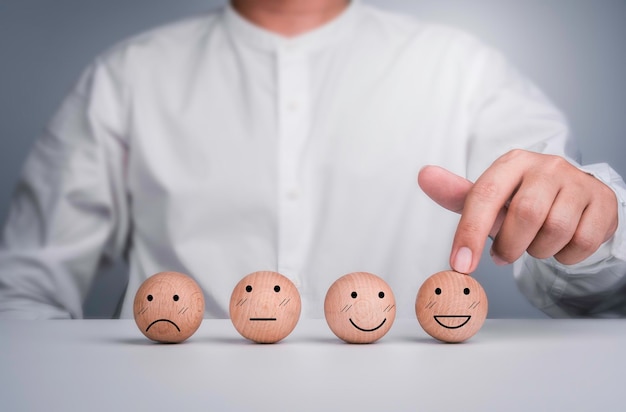 Фото Клиент-бизнесмен, показавший лучший рейтинг, выбрал счастливое лицо, смайлик, деревянный шар, отзывы об оценке обслуживания клиентов.