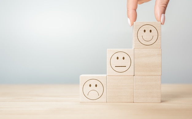 Customer service evaluation and satisfaction survey concepts. client hand picked happy face smile face symbol on wooden blocks, copy space, gray background