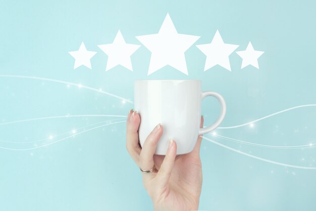 Concetti di valutazione del servizio clienti e indagine sulla soddisfazione. tazza di caffè del mattino della tenuta della mano della ragazza con l'icona del segno di valutazione di cinque stelle 5 su fondo blu. recensione, valutazione, soddisfazione.