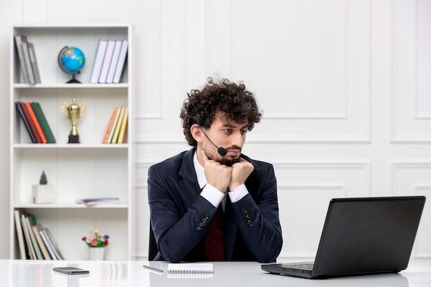 Customer service handsome young guy in office suit with laptop and headset with hands on chin