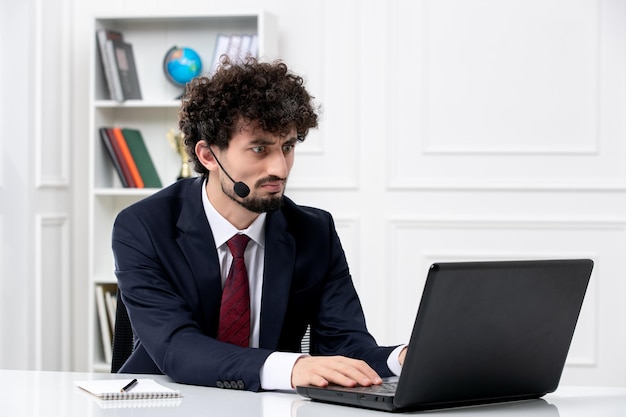 Customer service handsome young guy in office suit with laptop and headset working on computer