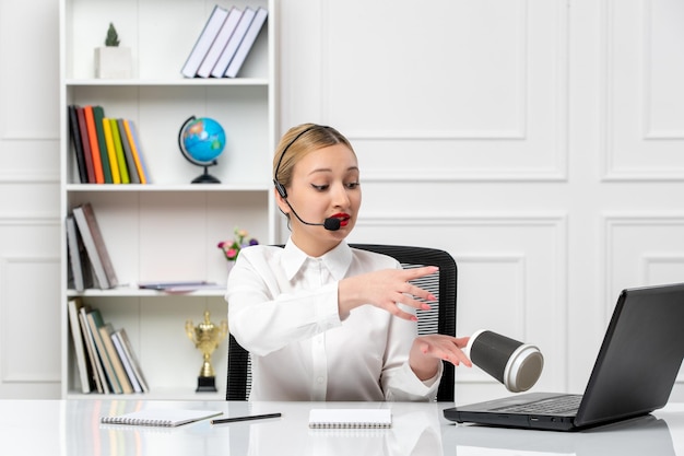 Customer service pretty blonde girl in white shirt and headset spilled coffee on computer