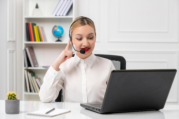 Customer service pretty blonde girl in white shirt with laptop and headset smiling while listening