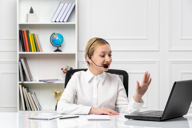 Customer service pretty blonde girl in white shirt with laptop and headset talking to a client