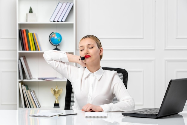 Customer service pretty blonde girl in white shirt with laptop and headset touching neck and tired