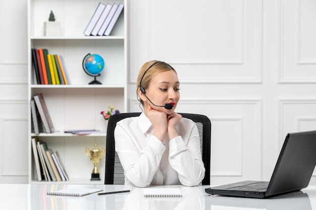 Customer service pretty blonde girl in white shirt with laptop and headset with hands on chin