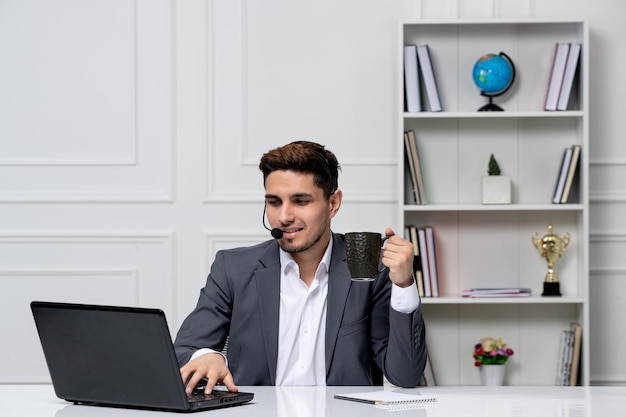 Customer service pretty gentleman with computer in grey office suit confidently holding coffee