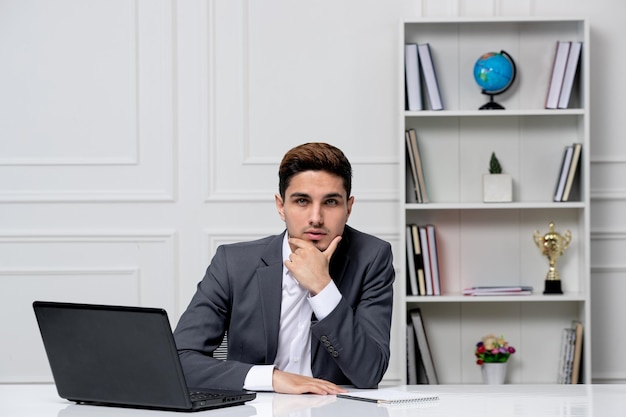 Customer service smart handsome guy with laptop in grey office blazer thinking looking serious