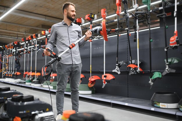 Photo customer with electric lawn trimmer in hands at garden equipment store