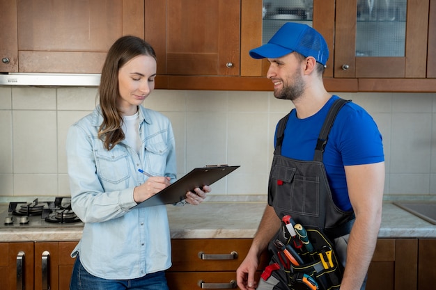 Customer woman signing invoice from male plumber standing in kitchen