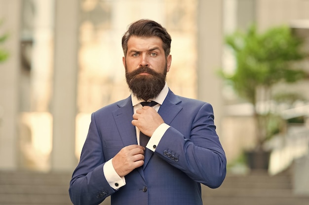 Customize your ensemble with tie Bearded man fix necktie wearing blue suit outdoors Classic fashion style Elegant formalwear Formal fashion Menswear Business outfit Attention to detail