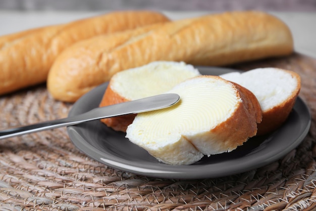 Cut baguette with fresh butter on wicker mat closeup