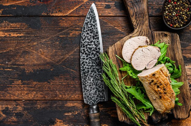 Cut baked pork tenderloin steak on a cutting board with arugula.