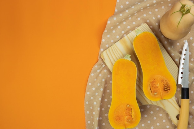 Cut of butternut squash on tablecloth with orange background