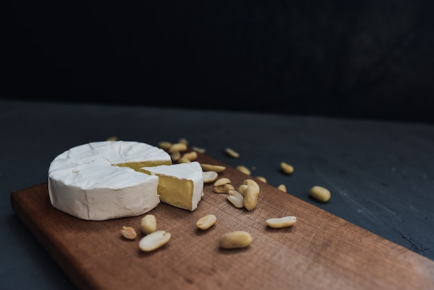 Cut Camembert cheese lies on a wooden kitchen plate with scattered peanuts