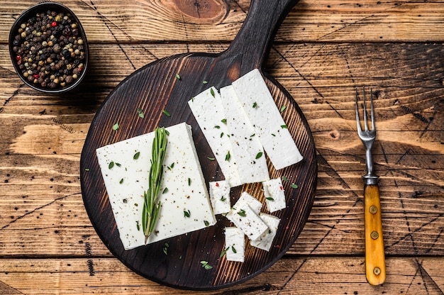 Photo cut cheese feta with rosemary on a wooden cutting board. wooden background. top view.