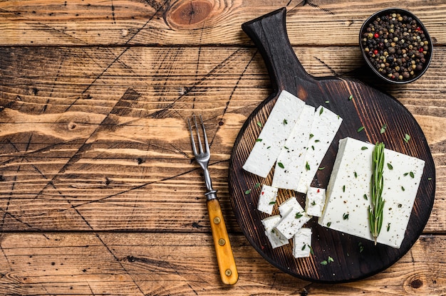 Tagliare la feta di formaggio con rosmarino su un tagliere di legno. tavolo di legno. vista dall'alto. copia spazio.