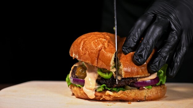 Cut craft burger is cooking on black background consist red\
sauce salsa lettuce red onion pickle cheese chilli green pepper air\
bun and marbled meat beef not made ideal loving hand made