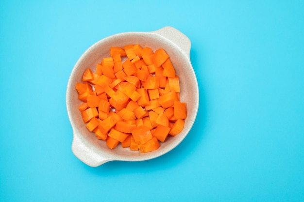 Cut cubes of fresh carrot in the bowl on blue