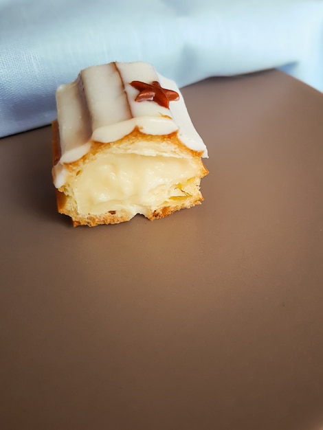 The cut of eclair with vanilla cream covered with white chocolate glaze on brown plate.