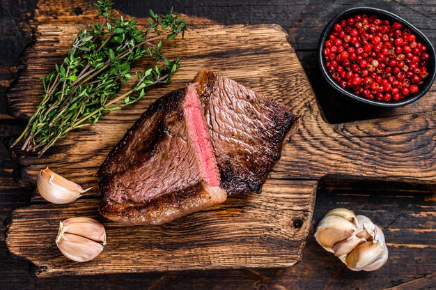 Cut fried rump cap or brazilian picanha beef meat steak on a wooden board on wooden table. Top view.