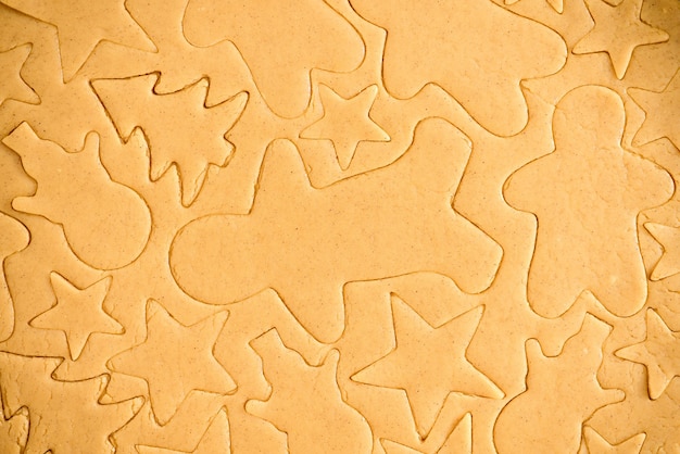 Cut gingerbread out of the dough using a gingerbread mold, top view, raw dough with cinnamon prepared for baking . the pattern on the dough of the figures.