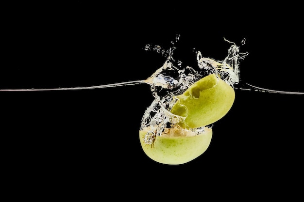 Cut green apple falling deep in water with splash isolated on black