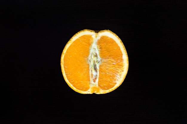 Cut half an orange on a wooden table on a dark background