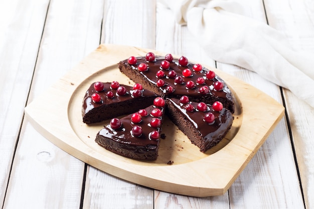 Cut into chunks of gluten-free Brownie cake with chocolate icing, decorated with cranberries, on a light wooden table. Healthy Desserts. Close-up