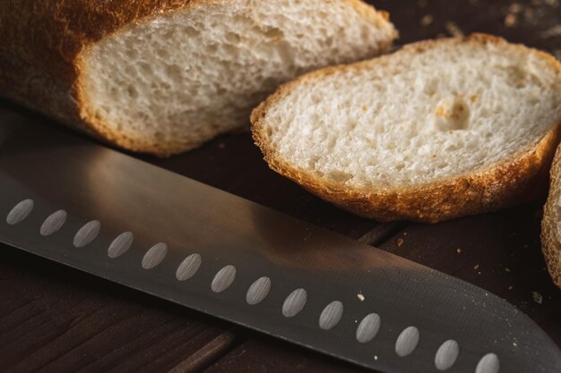 Cut into pieces fresh loaf of wheat grain bread slices of\
french baguette and knife closeup photo