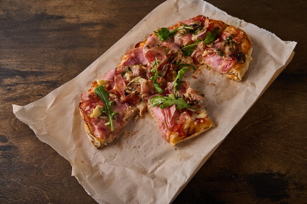 Cut into pieces rectangular roman pizza with prosciutto ham\
tomatoes mozzarella and arugula on on