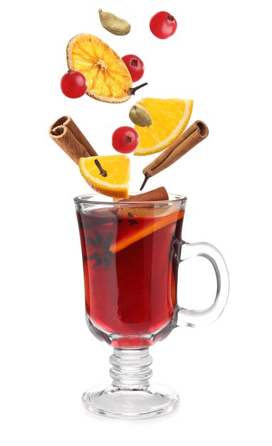 Cut orange cranberries and different spices falling into glass cup of mulled wine on white background