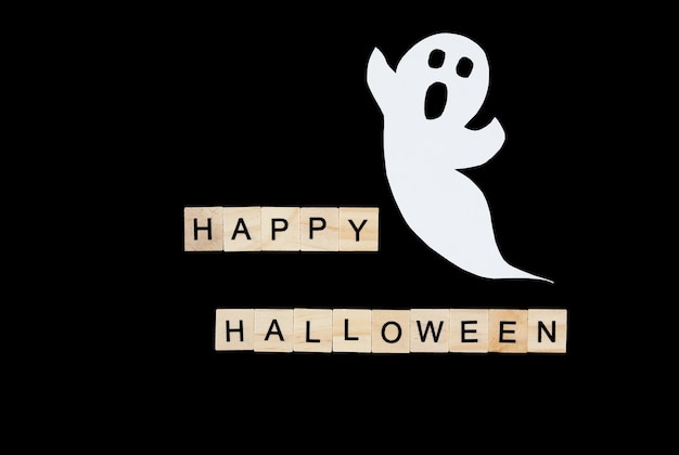 Ritaglia il fantasma di carta e le lettere di legno happy halloween sul nero.