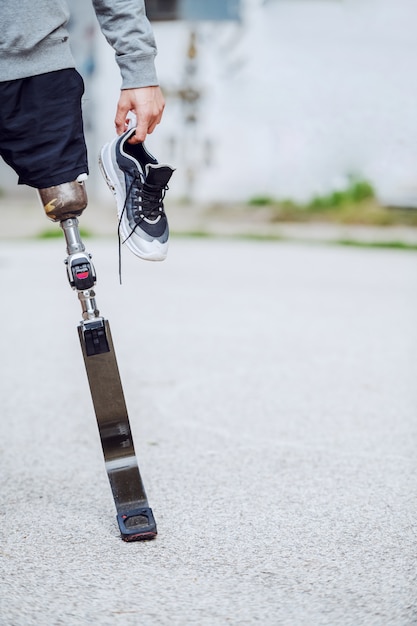 Cut out picture of caucasian handicapped sporty man standing outdoors with sneaker in hand.