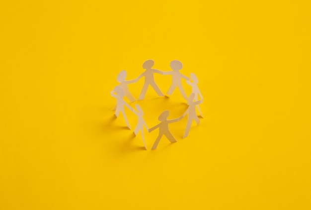 Cut paper human chain hold hands and show their unity on yellow background Solidarity and peace