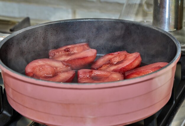 Cut pears are boiled in red syrup with wine on gas stove.