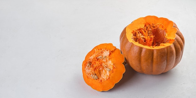 A cut but not peeled pumpkin with seeds on a gray background