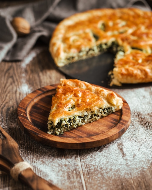 Cut pie with spinach and cheese filling on the wooden table