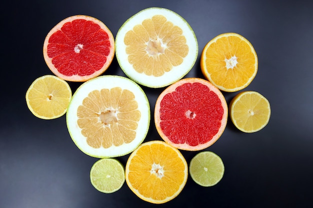 Cut pieces of different citrus fruits on dark space