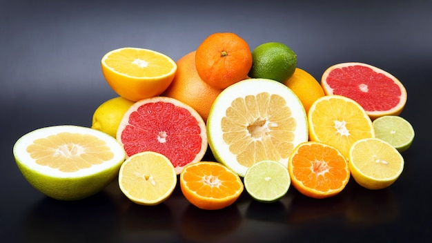 Cut pieces of different citrus fruits on dark space