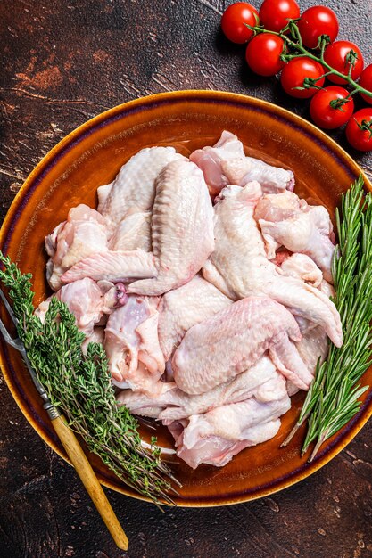 Cut Raw chicken wings in a rustic plate with thyme and rosemary. Dark background. Top view.