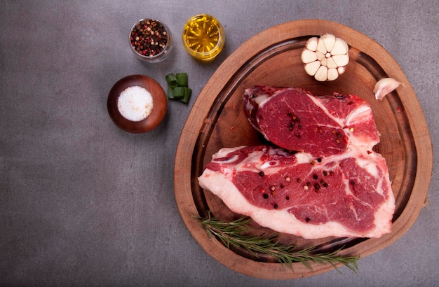 Cut of raw meat with fat tbone steak in the butcher's shop on wooden board with seasonings garlic olive right side