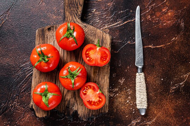 Cut Red cherry tomatoes on wooden cutting  board. Dark background. Top view.